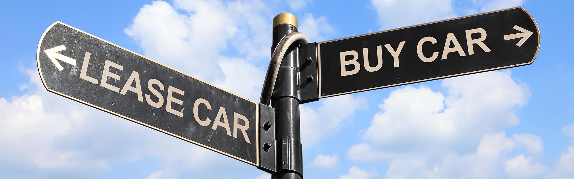 A directional street sign pointing left towards "LEASE CAR" and right towards "BUY CAR" against a blue sky with clouds.
